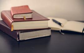 Three books stacked with one open book next to a pen