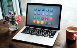Laptop on a desk, next to a small clear vase with flowers