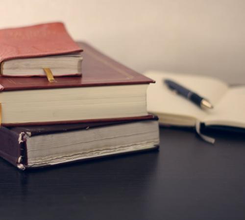 Three books stacked with one open book next to a pen