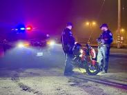 Two Lathrop Police officers examine a dirt bike. A police SUV with lights is visible in the background
