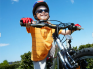 A young boy wearing a helmet smiles as he sits on a bicycle