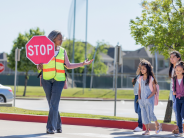 A woman wearing a reflective vest holds a stop sign as a group of children crosses the road