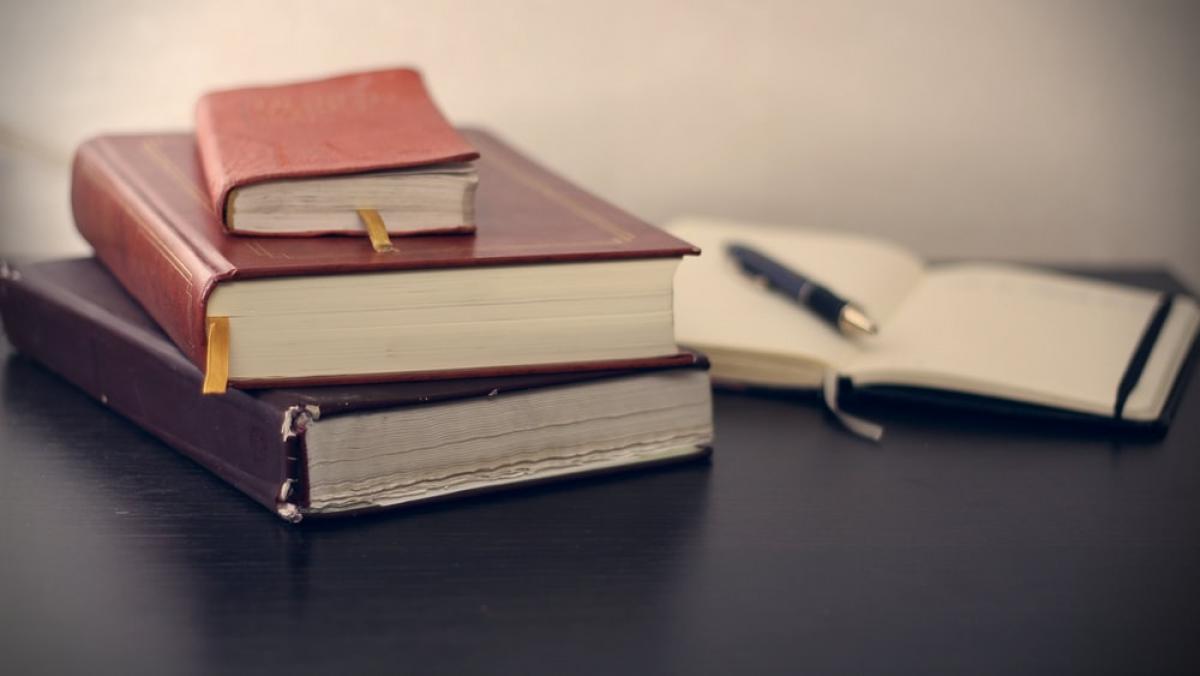 Three books stacked with one open book next to a pen